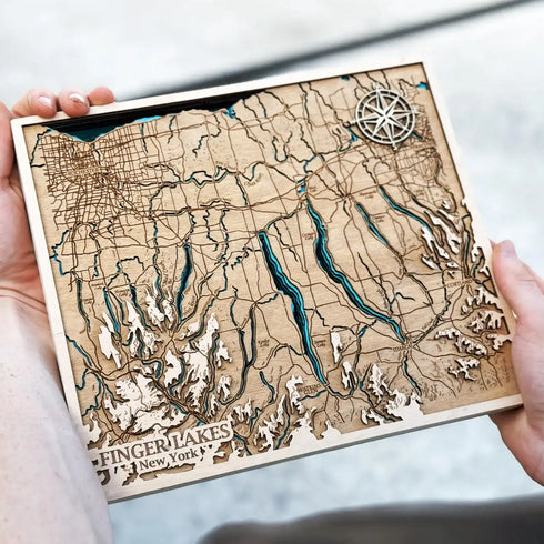 Hand holding detailed laser-cut wooden map of Finger Lakes region